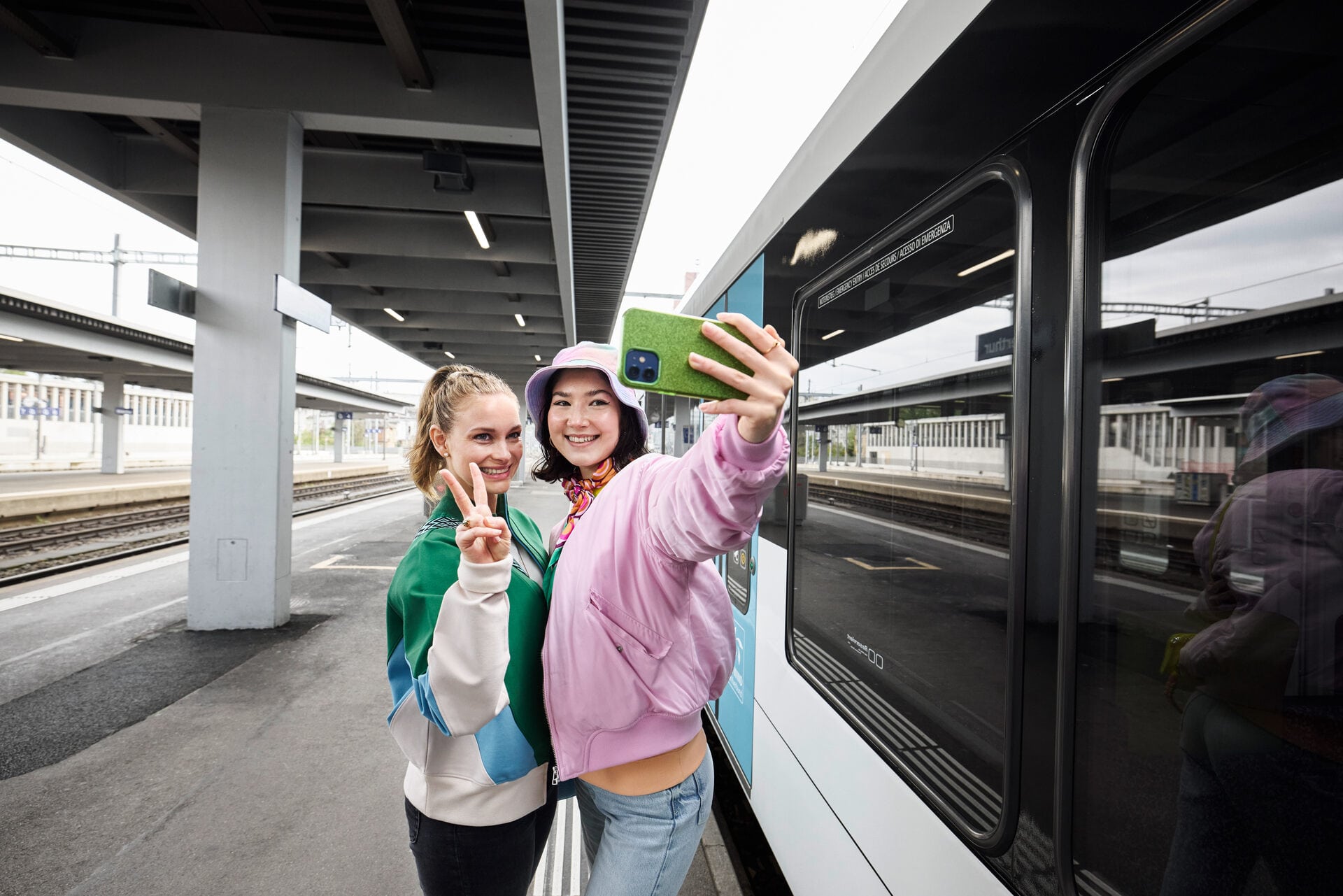 Zwei lächelnde Teenagerinnen machen am Bahngleis ein Selfie, das als Symbolbild für das Thema Abofalle dient.