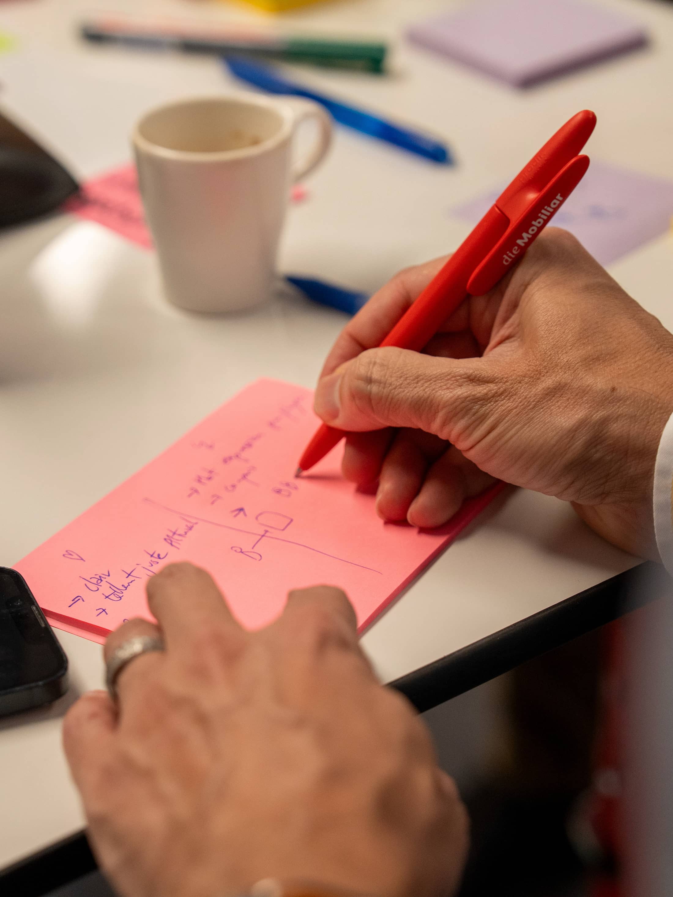 Foto dettagliata: mano che tiene una penna e scrive su un post-it durante il workshop «Plasmare il futuro». 