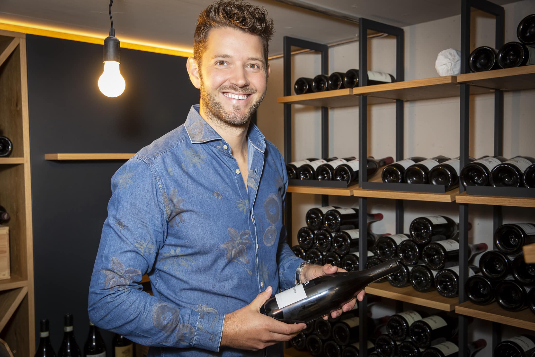 Adrian Weibel in cantina, con una bottiglia di vino in mano.